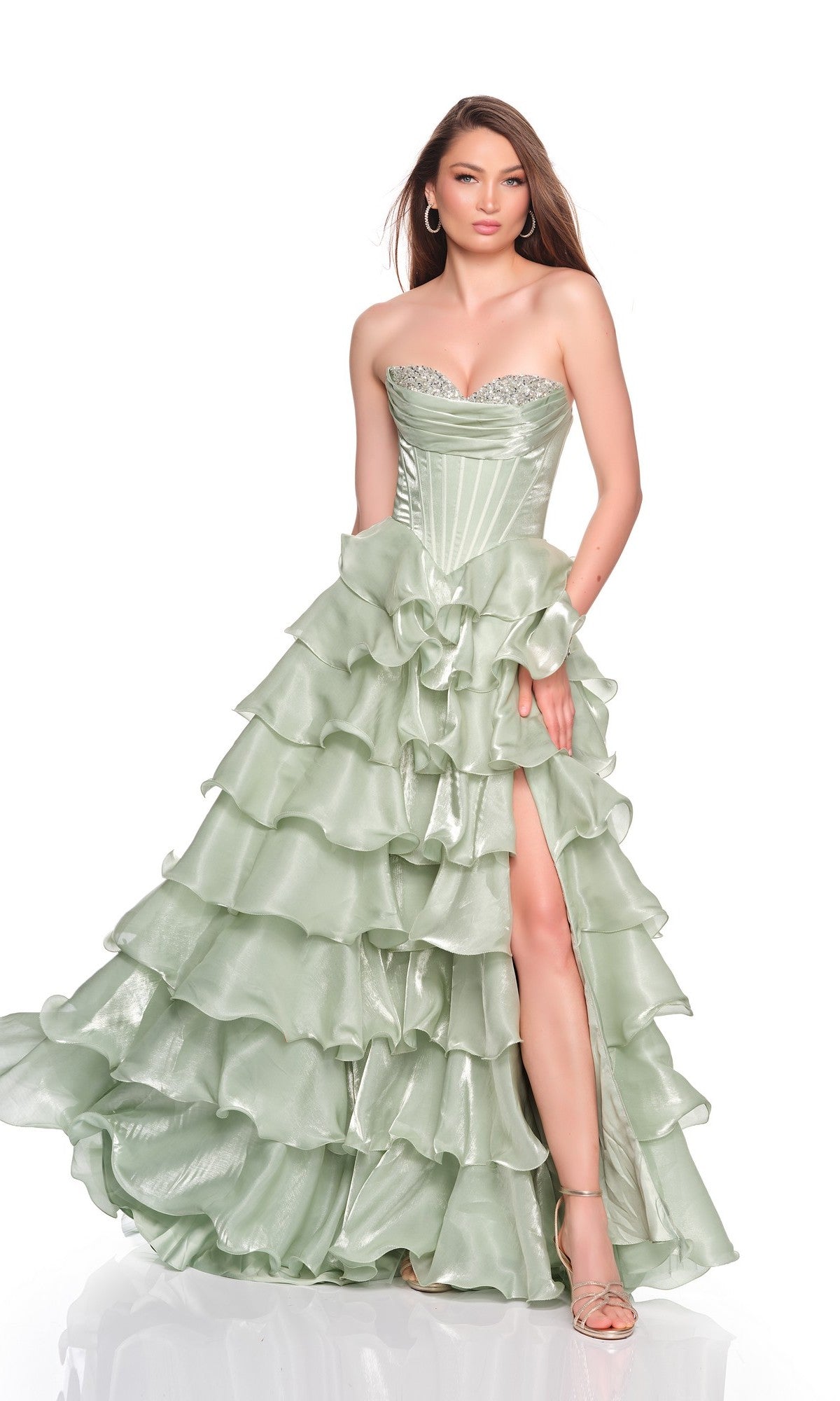 A woman wearing the Dave and Johnny 12777 long prom dress in strapless green organza with ruffle tiers and a high slit stands against a plain white background.